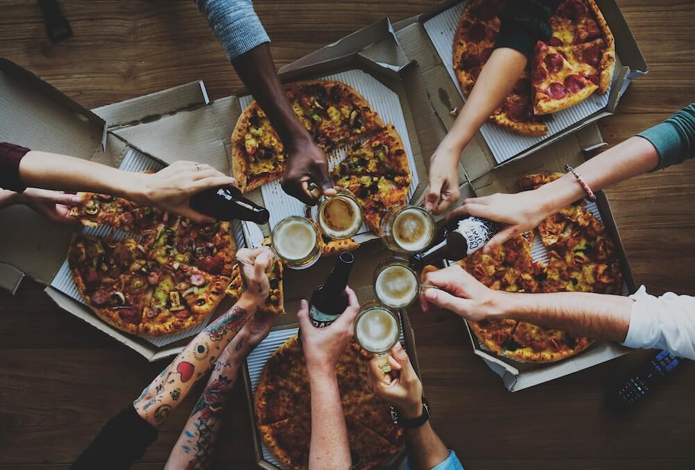 people together eating pizza and cheering drinks